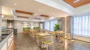 A modern dining area with wooden chairs and tables, a kitchen in the background, and a large window with curtains. - Yihe Hotel (Dongguan)