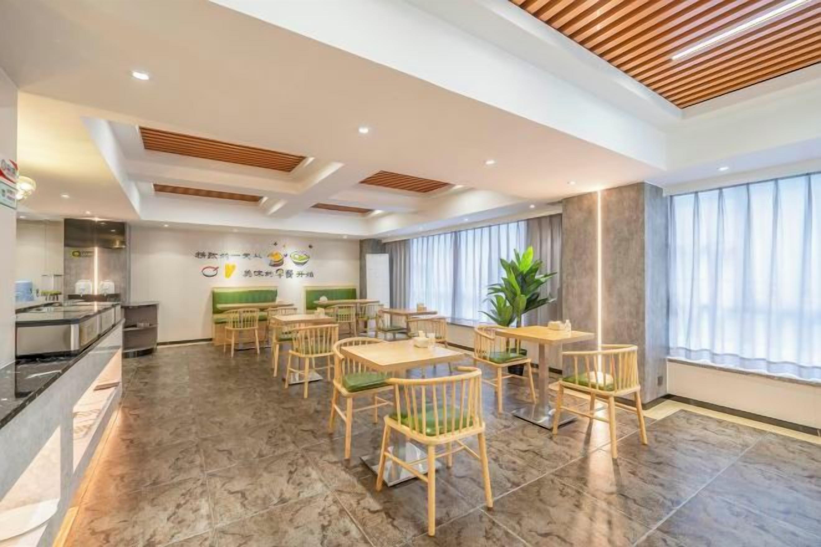 Een restaurantgedeelte in een hotel met verschillende tafels en stoelen, een keuken op de achtergrond en een groot raam met gordijnen.