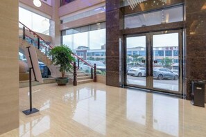 A spacious lobby with a polished floor, a staircase, and a large window offering a view of parked cars and buildings outside. - Yihe Hotel (Dongguan)