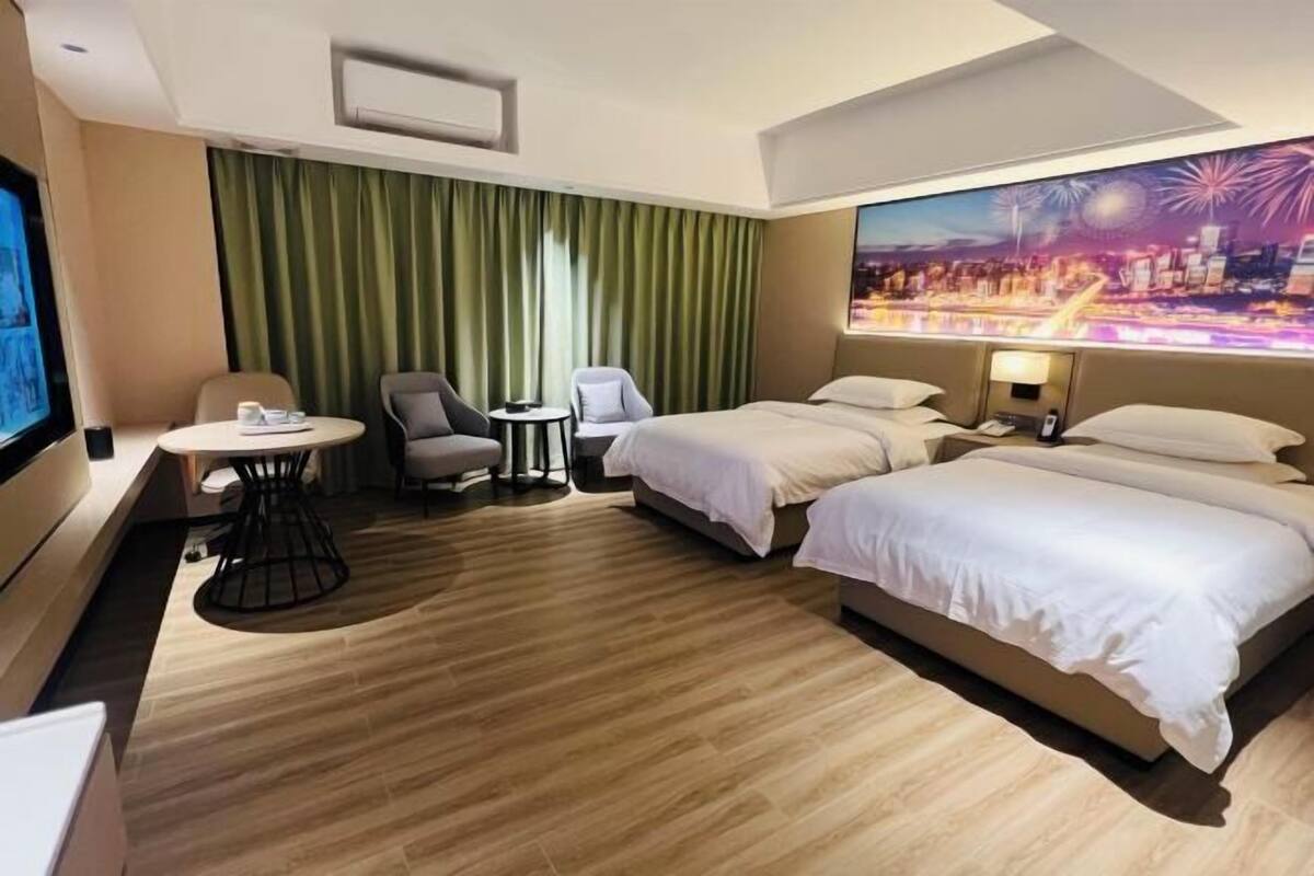 A hotel room with a bed, two chairs, a small table, a TV, and a curtain.