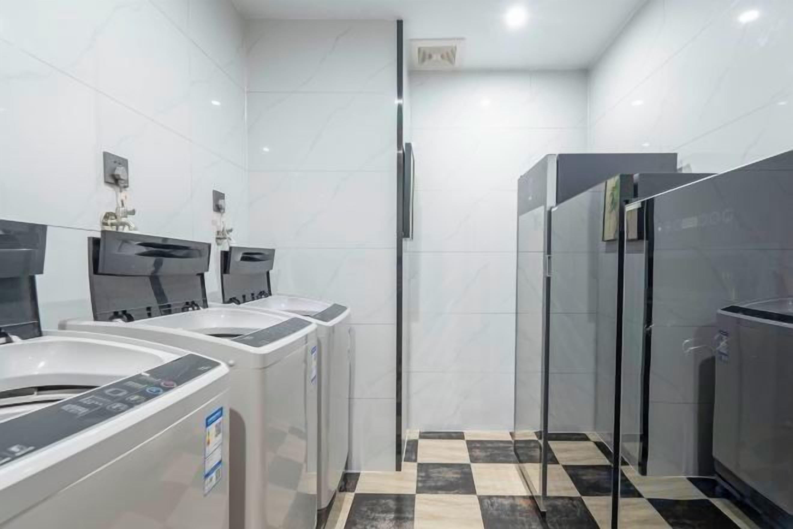 Ein modernes Badezimmer mit einem schwarz-weißen Schachbrettfußboden, einer Duschkabine aus Glas und einer Reihe weißer Waschbecken mit schwarzen Wasserhähnen.