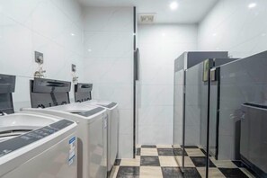 A modern bathroom with a black and white checkered floor, a glass shower enclosure, and a row of white sinks with black faucets. - Yihe Hotel (Dongguan)