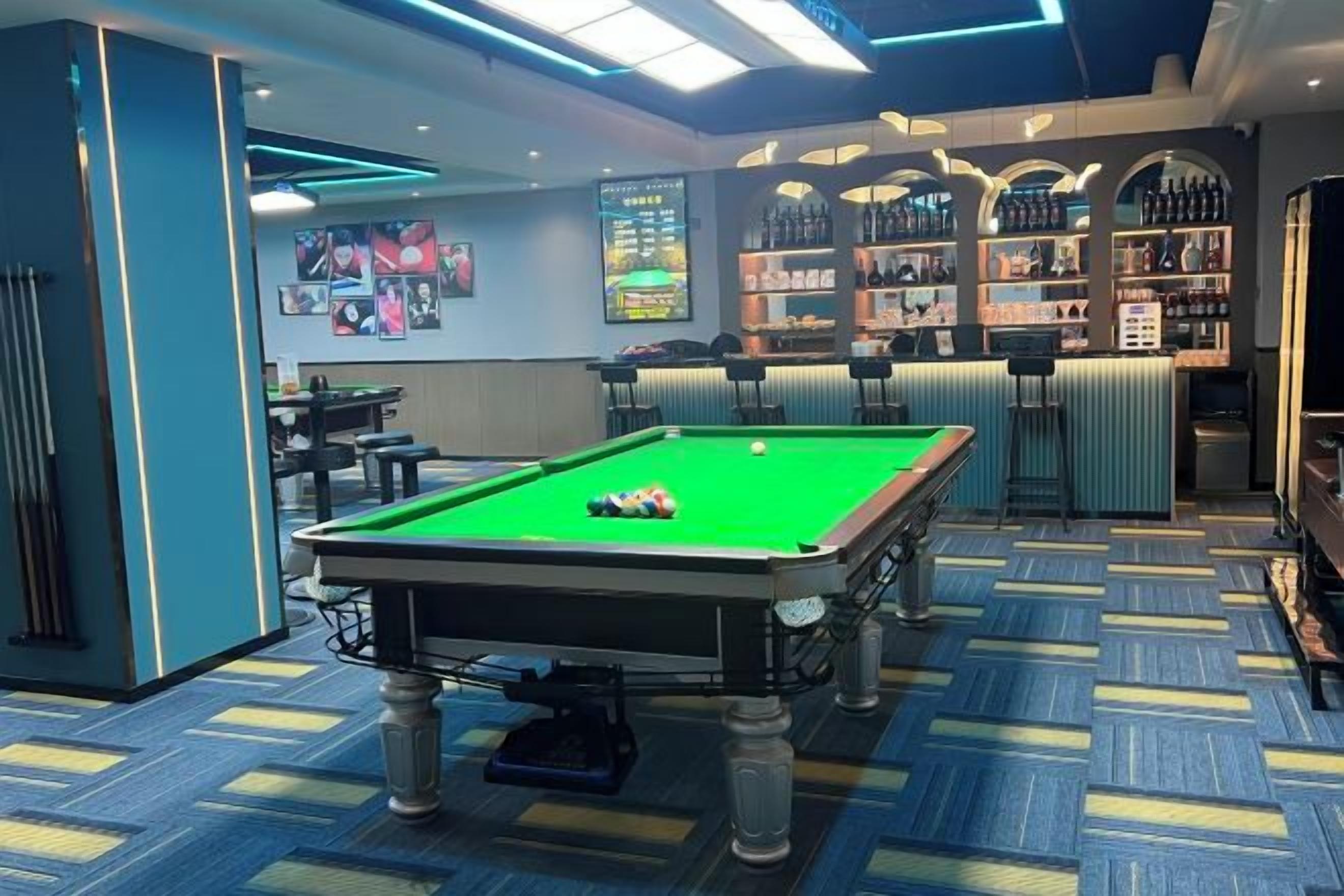 A pool table with a cue ball, a bar area with shelves of bottles, and a patterned carpet.