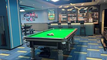 A pool table with a cue ball, a bar area with shelves of bottles, and a patterned carpet.