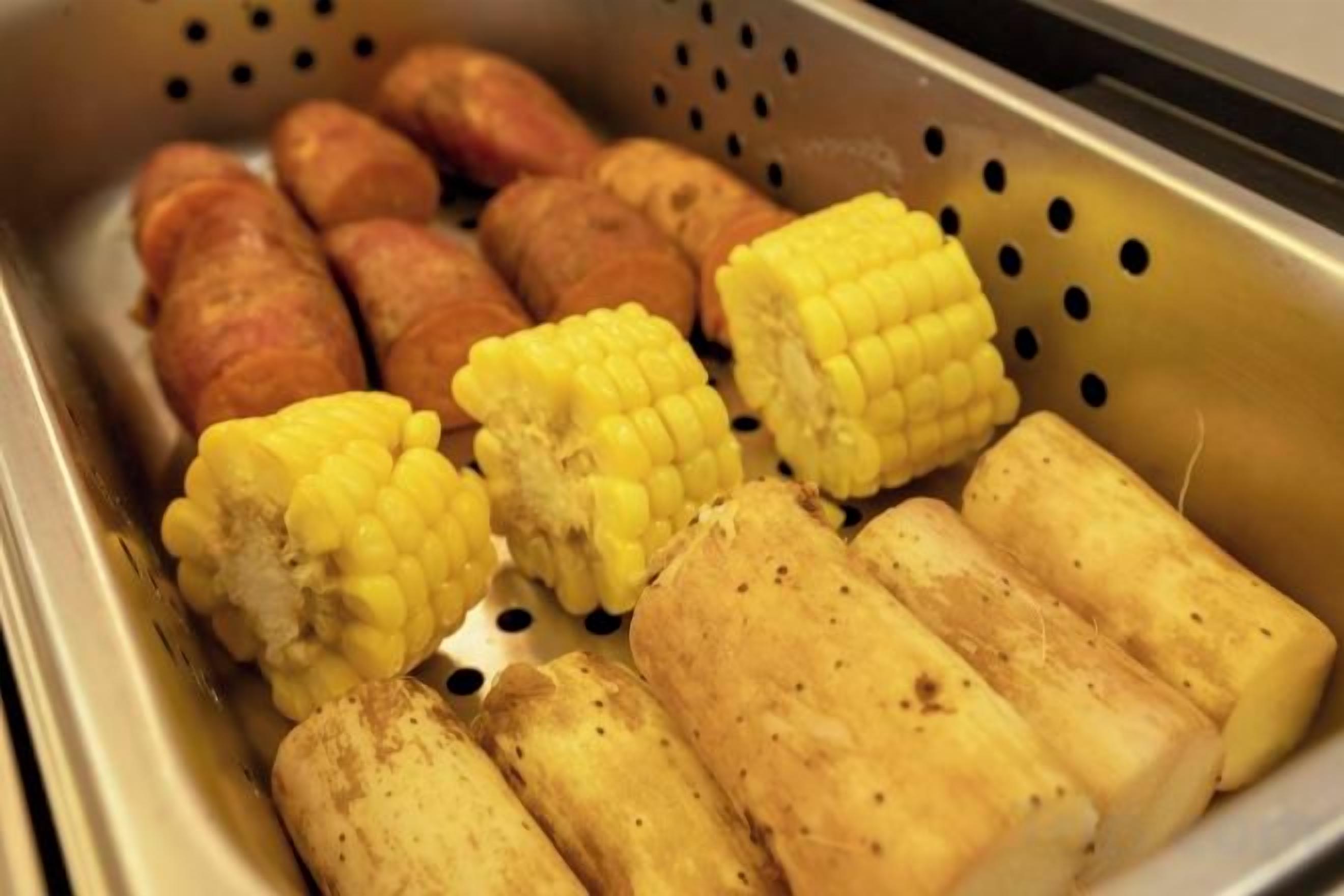 A colander containing corn on the cob and sausages.