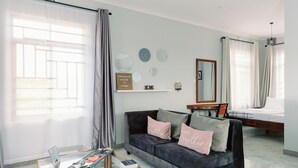A modern living room with a dark grey sofa, a glass coffee table, and a bed in the background. - Cozy studio suite with a full kitchen and sitting area (Arusha)
