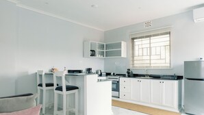 A modern kitchen with white cabinetry, a built-in island, and a window with blinds. - Cozy studio suite with a full kitchen and sitting area (Arusha)