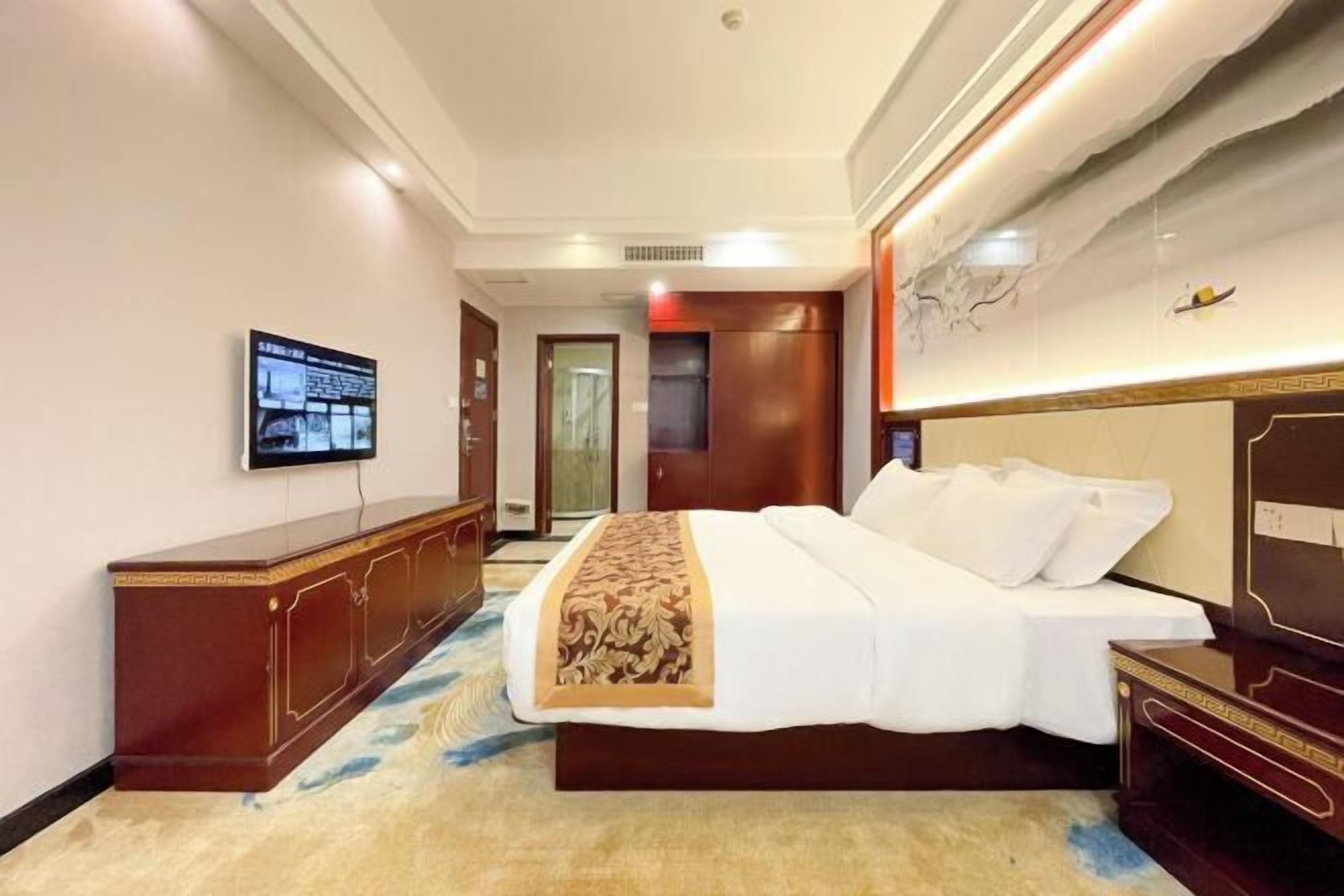 Une chambre d’hôtel avec un lit, un téléviseur fixé au mur, une commode en bois et un sol recouvert de moquette.