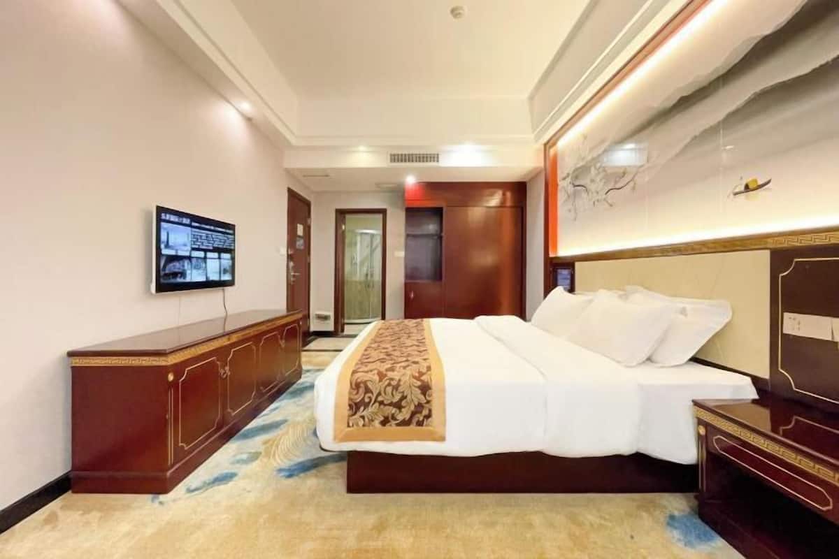 A hotel room with a bed, a TV mounted on the wall, a wooden dresser, and a carpeted floor.