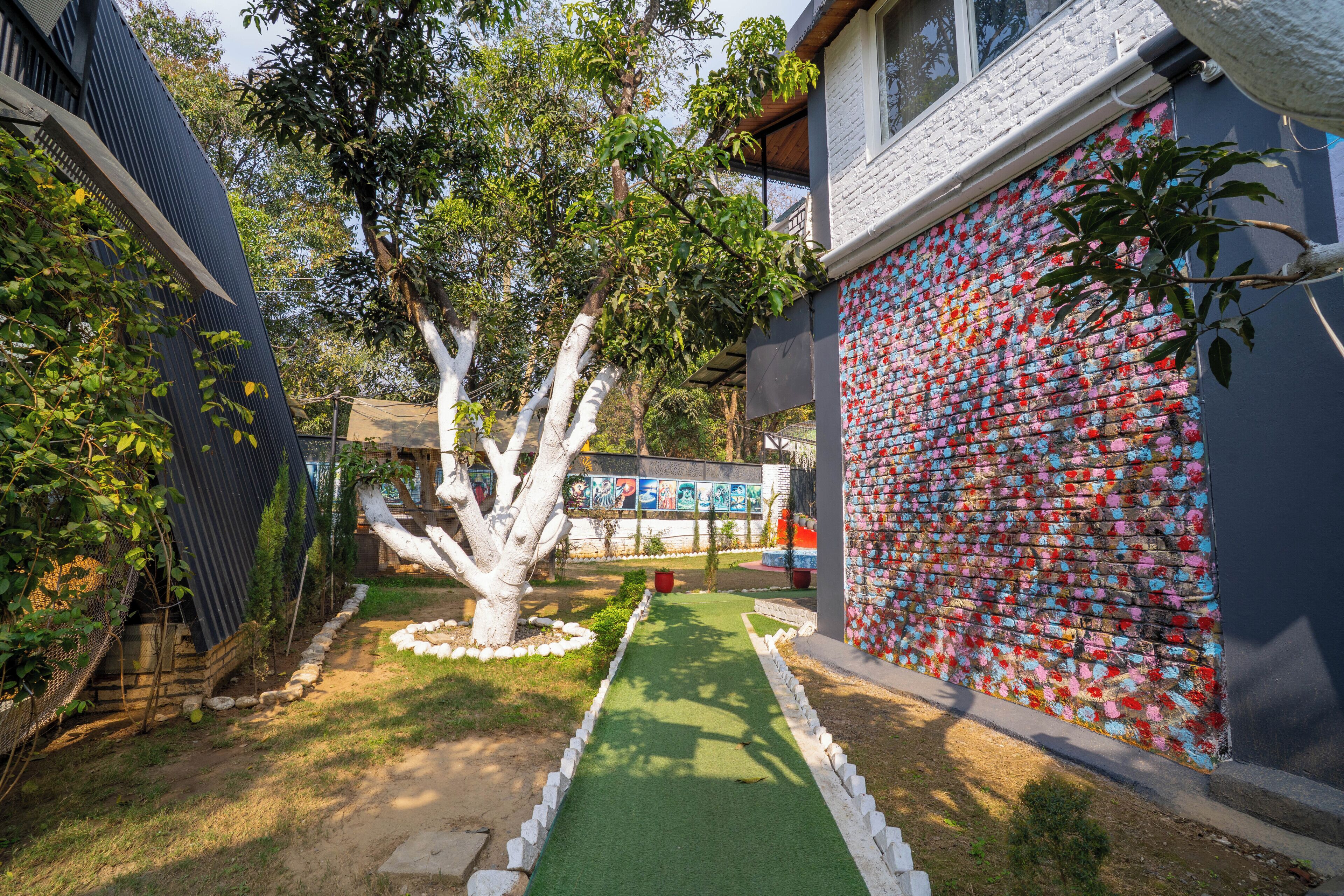 A garden with a green pathway, a white tree, and a wall covered in colorful tiles.