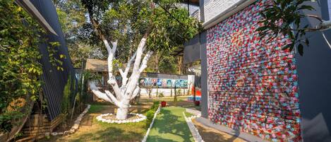 A garden with a green pathway, a white tree, and a wall covered in colorful tiles.