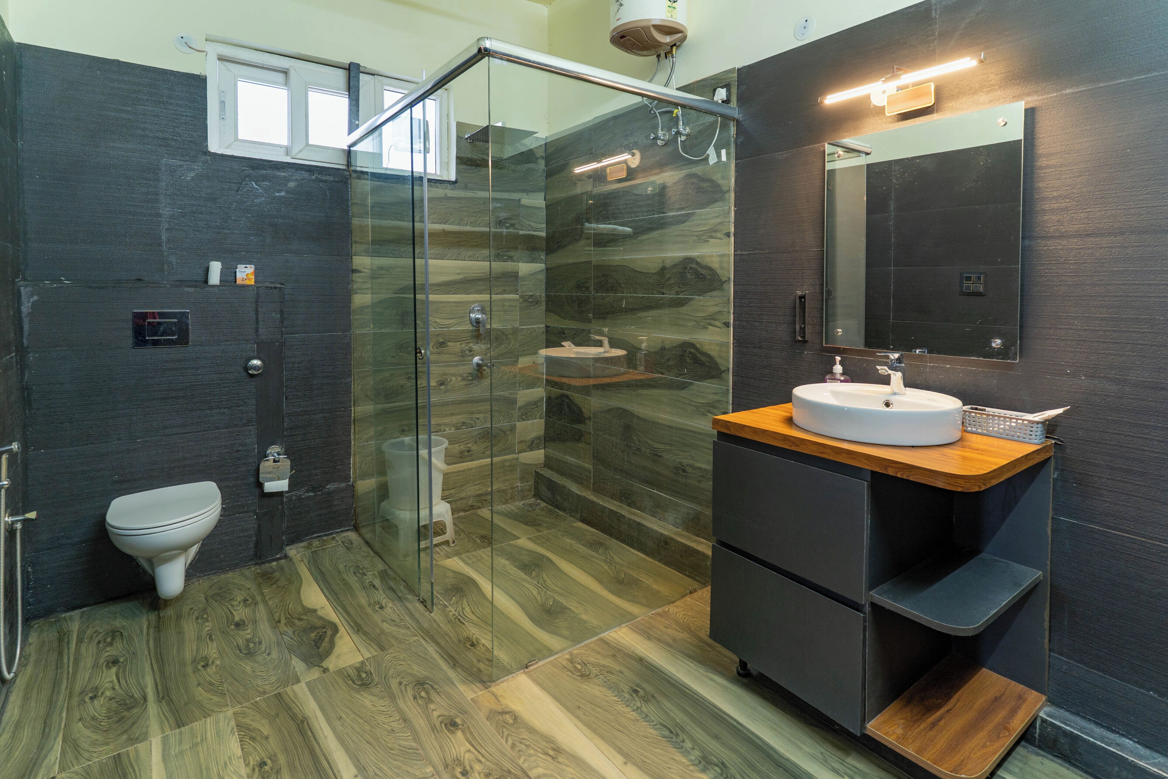 A modern bathroom with a glass shower enclosure, a white toilet, a wooden vanity with a sink, and a large mirror.