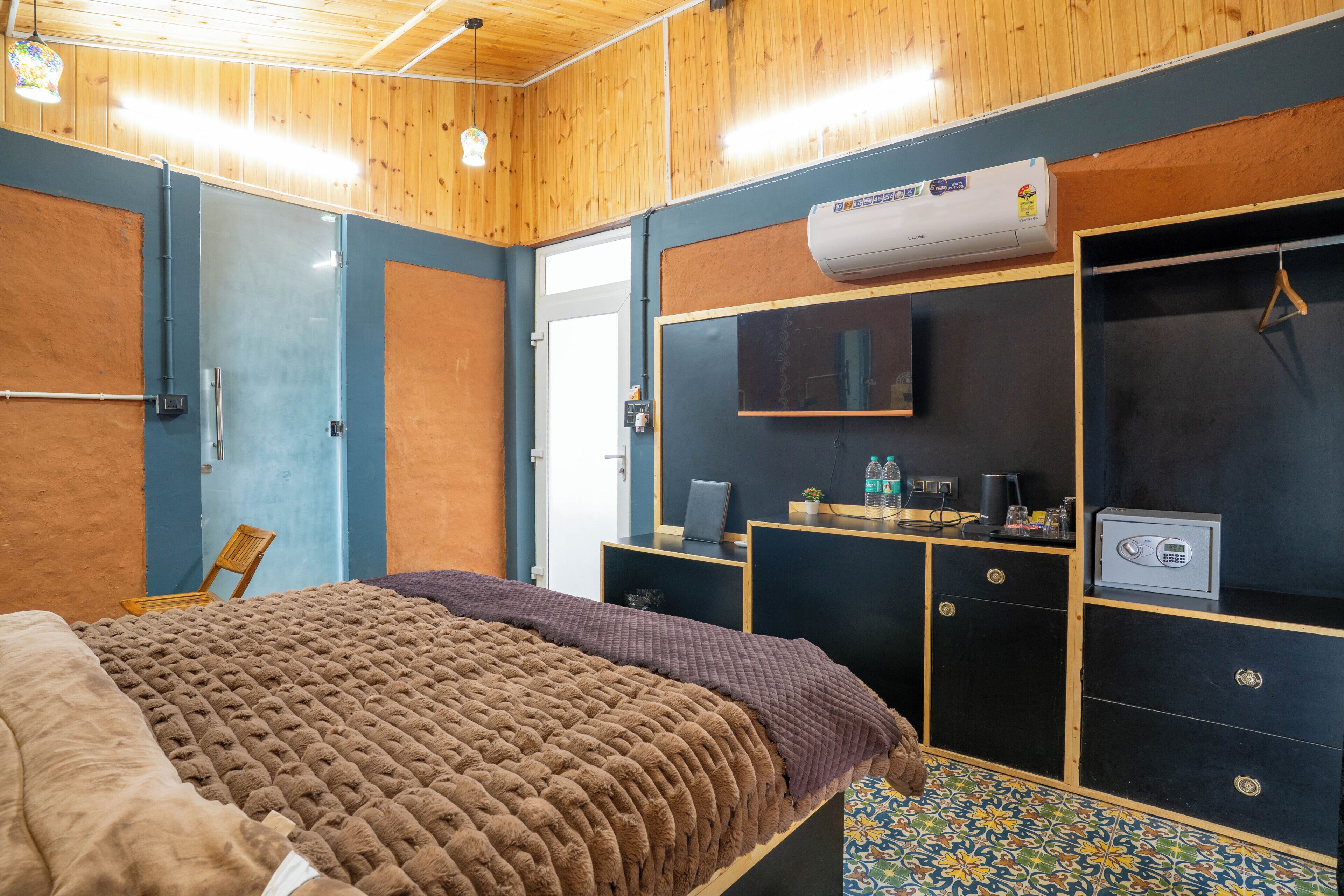 A bedroom with a bed, a desk, a wardrobe, and an air conditioning unit.