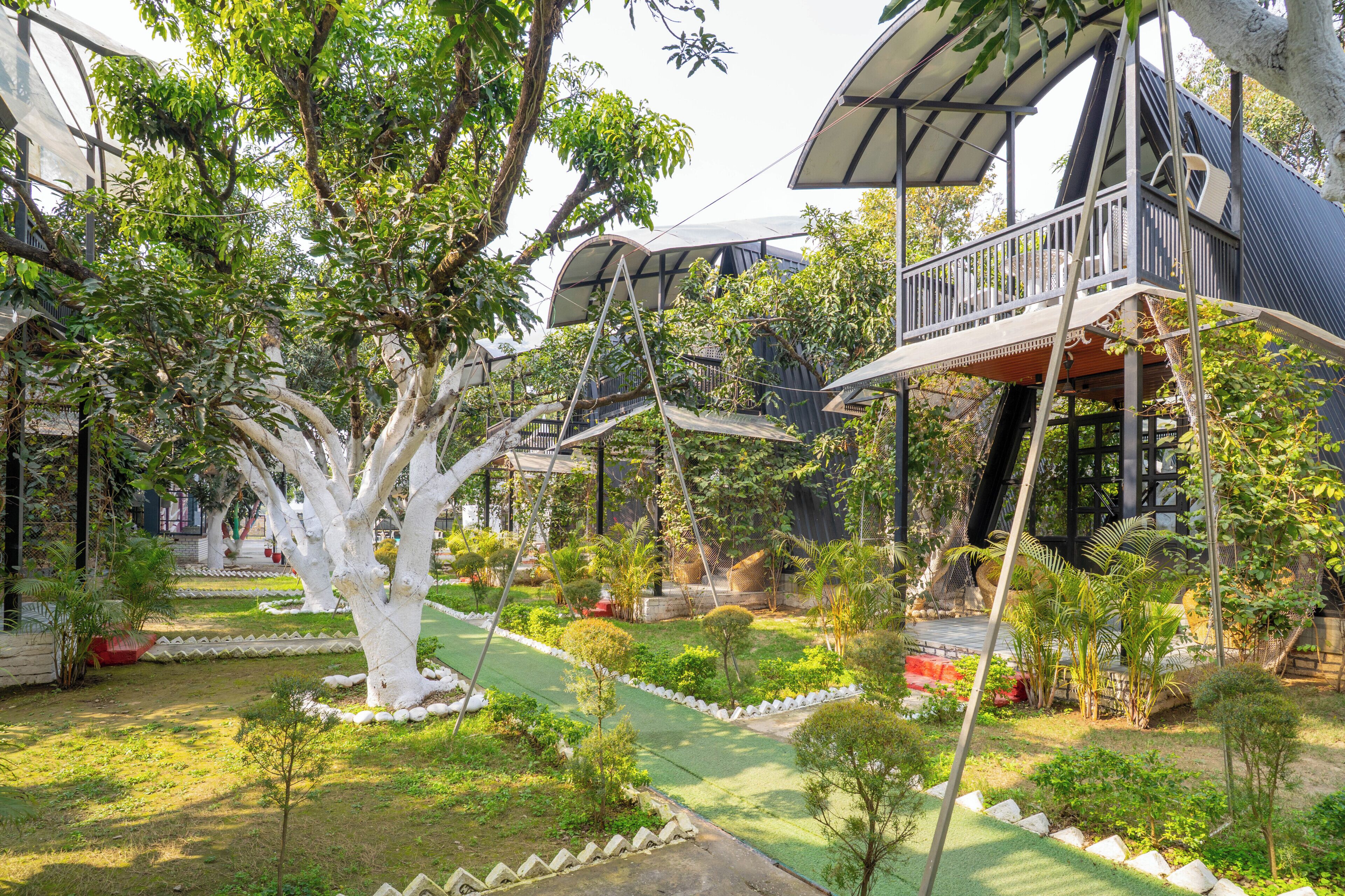 Une cabane perchée dans un arbre, dotée d’un balcon, entourée d’une végétation luxuriante et d’un jardin bien entretenu.