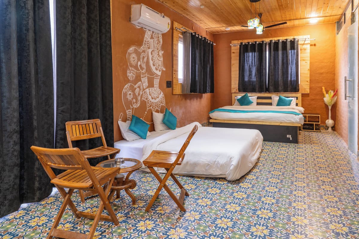 Ein Zimmer mit einem Bett, zwei Holzstühlen, einem kleinen Tisch, einem Spiegel und einem fußbodenbepflasterten Boden.