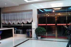 Un hall de hotel con mostrador de recepción, una planta en maceta y puerta de vidrio de entrada.
