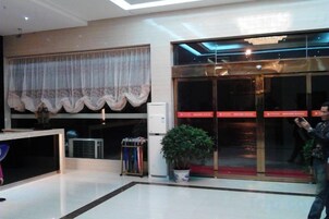 Un hall de hotel con mostrador de recepción, una planta en maceta y puerta de vidrio de entrada.