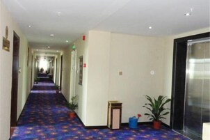 Un pasillo de hotel con alfombra estampada, plantas en macetas y una puerta a la derecha.