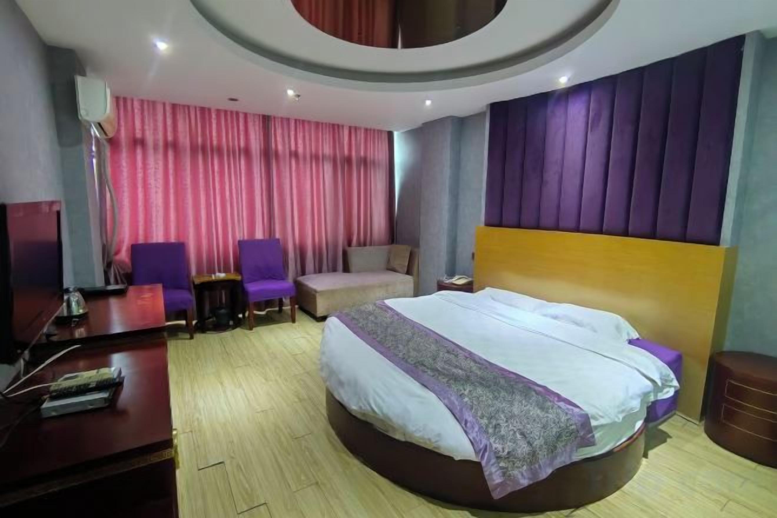 A hotel room with a large bed, two armchairs, a desk, and a television.