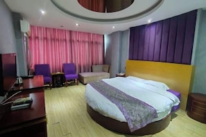 Una habitación de hotel con una cama grande, dos sillones, un escritorio y una televisión.