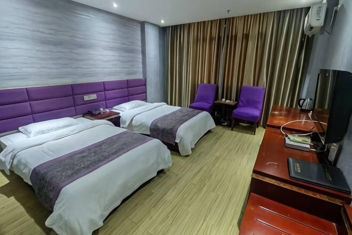 A hotel room with two beds, a desk, a chair, and a television.