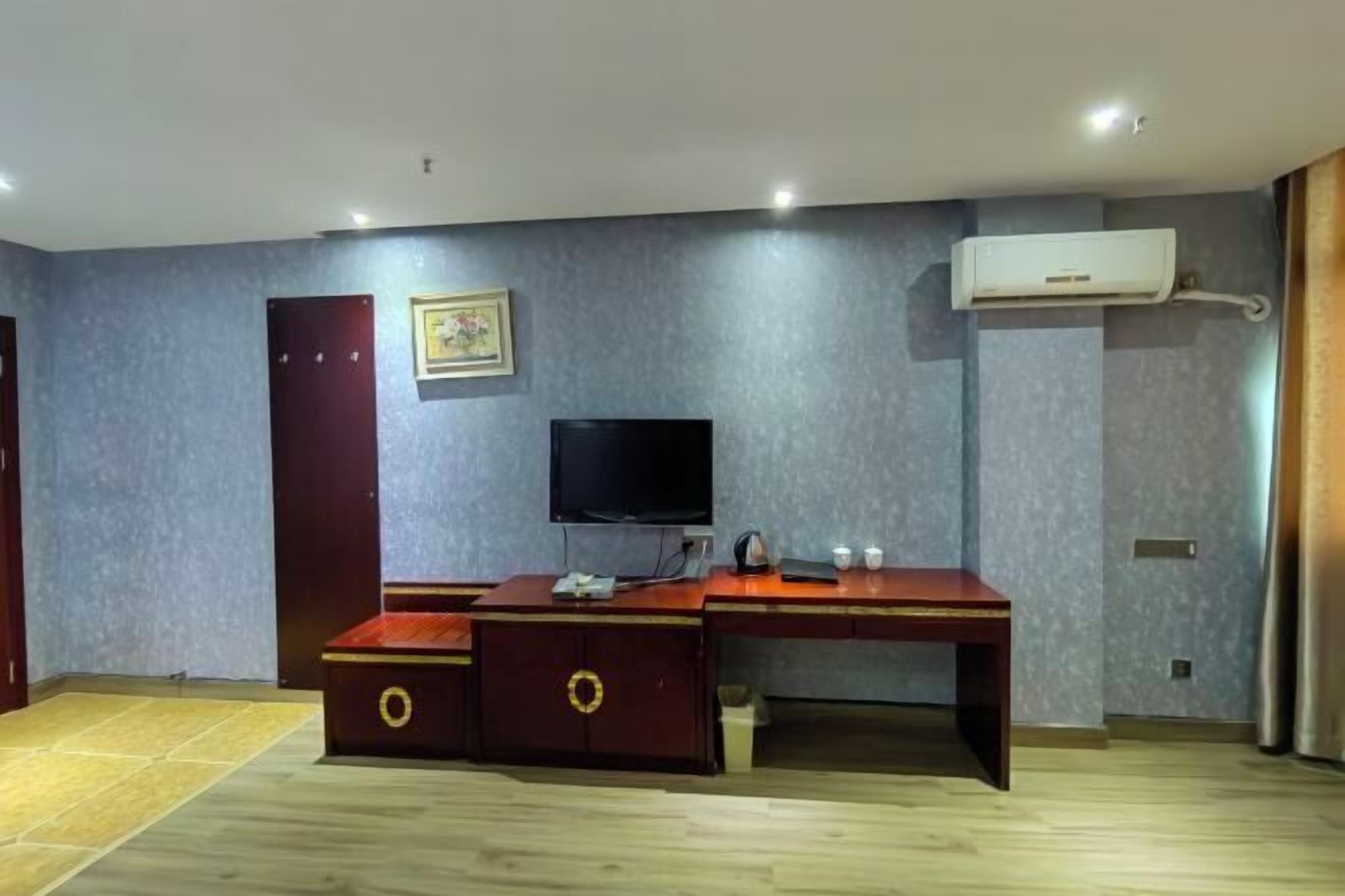 A room with a desk, a television, a wardrobe, and an air conditioning unit.