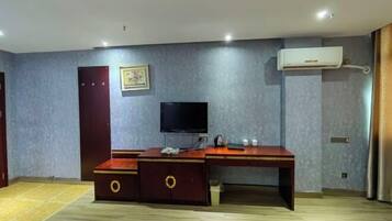 A room with a desk, a television, a wardrobe, and an air conditioning unit.