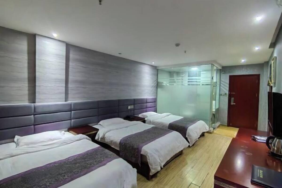 A hotel room with three beds, a wooden floor, a red door, and a television on a wooden table.