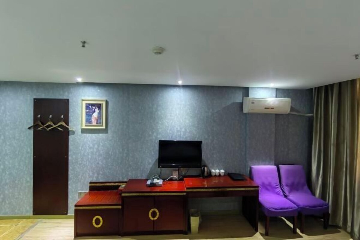 Una habitación de hotel con escritorio, una silla morada, televisor y aire acondicionado.