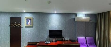 Ein Hotelzimmer mit Schreibtisch, einem violetten Sessel, einem Fernseher und einer Klimaanlage.