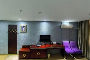 Una habitación de hotel con escritorio, una silla morada, televisor y aire acondicionado.