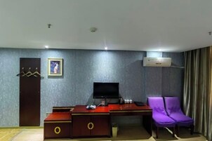 Una habitación de hotel con escritorio, una silla morada, televisor y aire acondicionado.