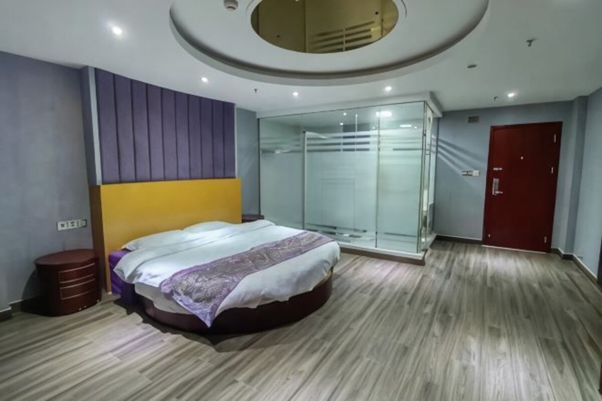 A modern bedroom with a bed, a glass shower, and a red door.