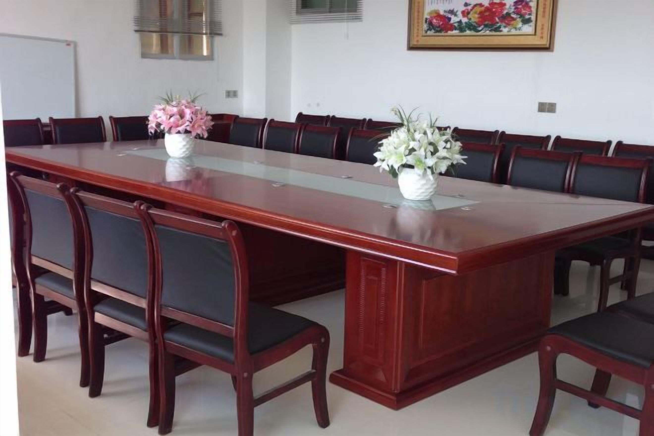 Un salón de conferencias con una larga mesa, varias sillas y dos jarrones de flores.