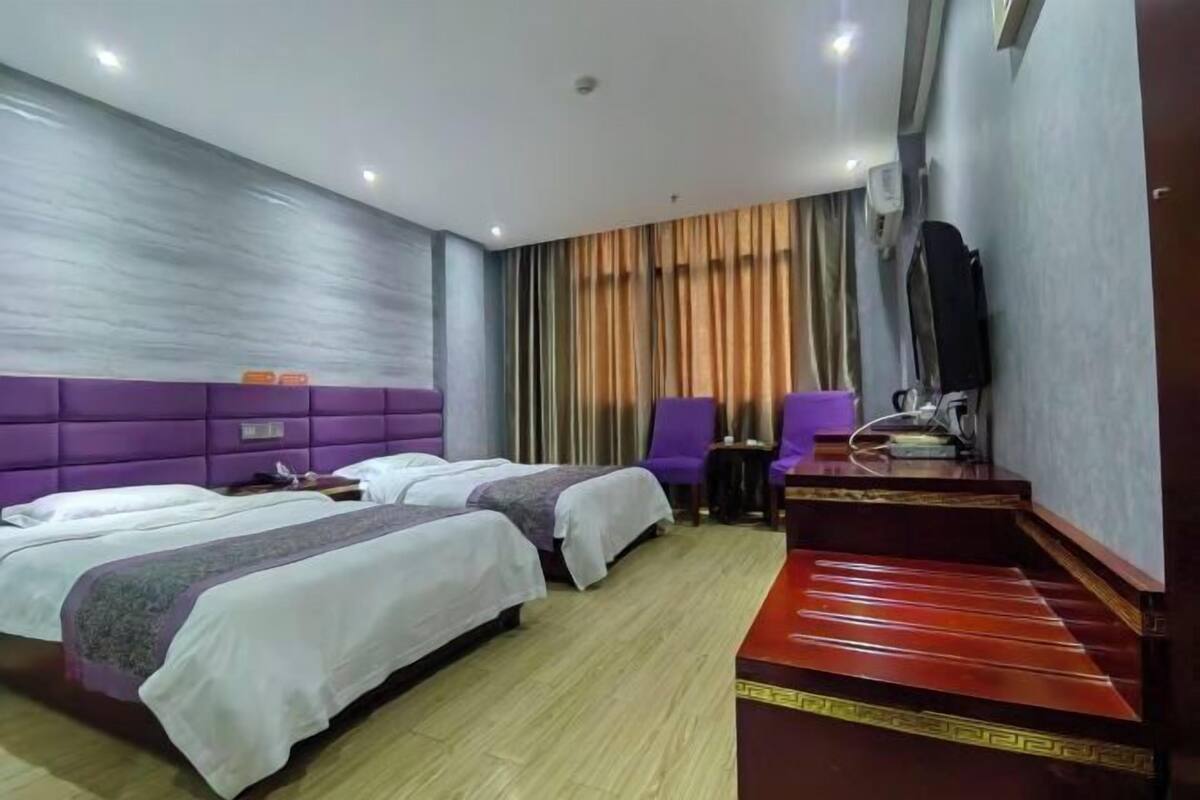 A hotel room with two beds, a desk, a chair, and a large window with curtains.