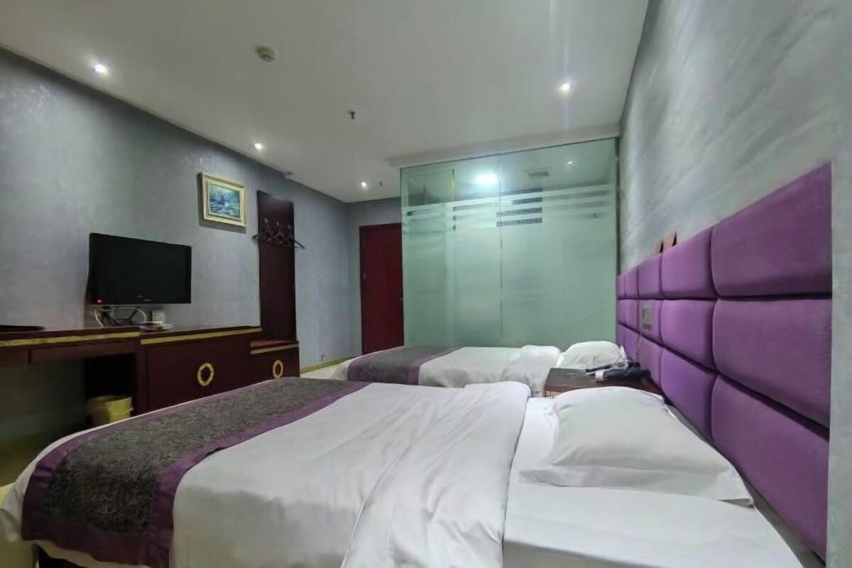 A hotel room with two beds, a TV, a wardrobe, and a glass partition.