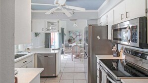 A modern kitchen with stainless steel appliances, a dishwasher, and a dining area with a table and chairs. - Modern 2 bedroom home with private pool & garage - Avalon (Englewood)