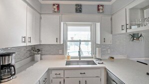 A modern kitchen with white cabinets, a stainless steel sink, and a window with a view of the outdoors. - Modern 2 bedroom home with private pool & garage - Avalon (Englewood)