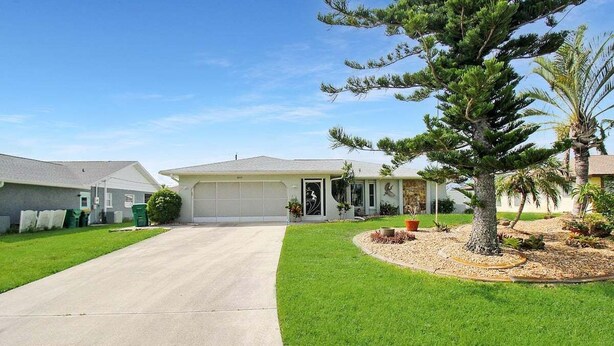A single-story house with a garage, a driveway, and a well-maintained lawn with a large tree and a palm tree. - Modern 2 bedroom home with private pool & garage - Avalon (Englewood)