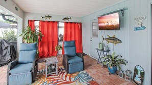 A cozy patio area with two blue cushioned chairs, a small table, and a TV mounted on the wall. - Modern 2 bedroom home with private pool & garage - Avalon (Englewood)