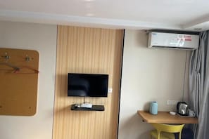A hotel room with a mounted TV, a desk with a kettle, a chair, and an air conditioning unit. - Qinyuanchun Hotel (Taizhou)