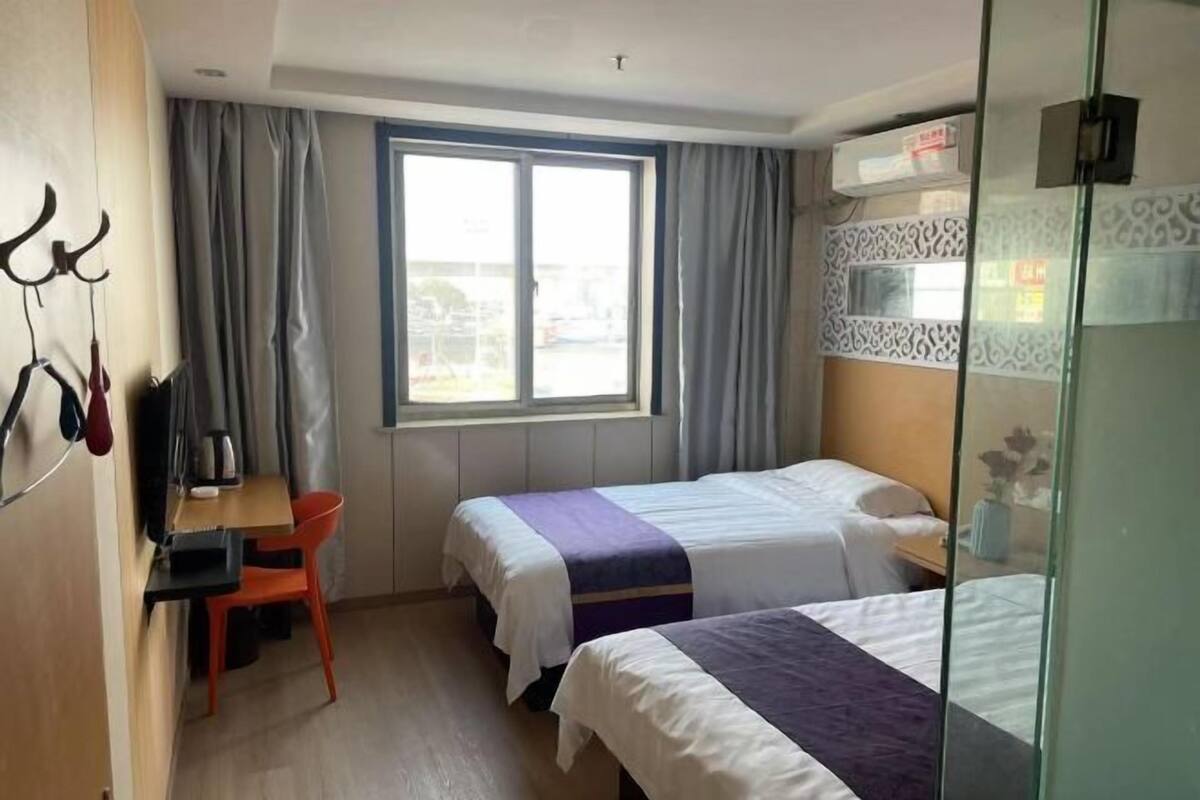 Habitación de hotel con dos camas, un escritorio, una silla, una ventana con cortinas y aire acondicionado instalado en la pared.
