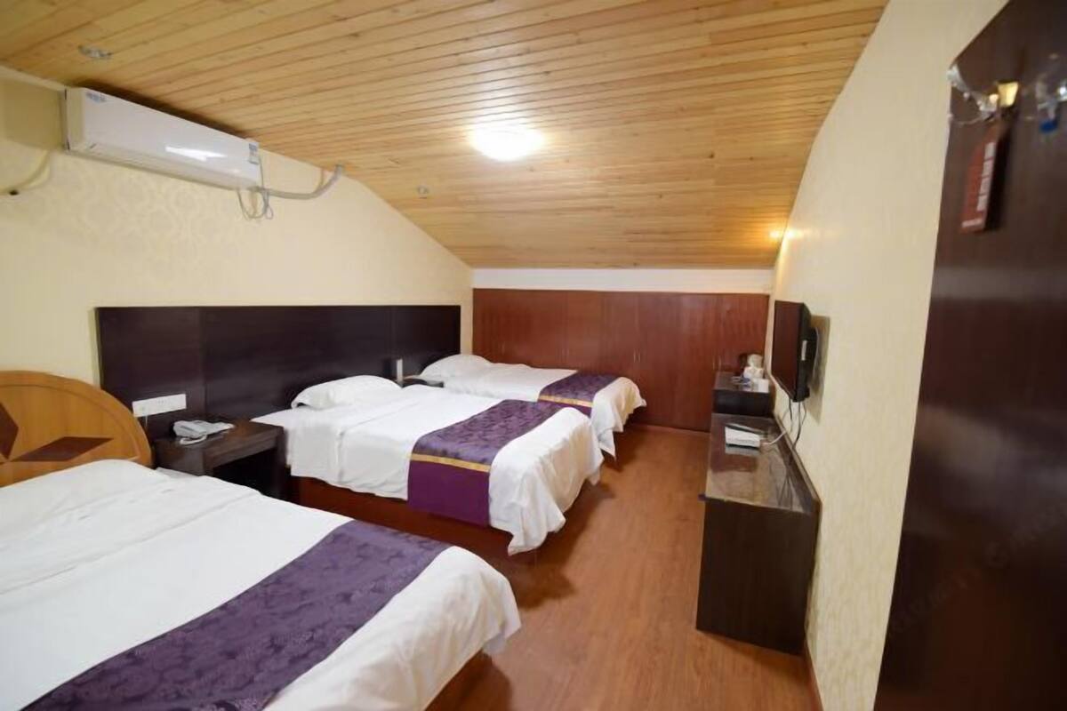 Habitación de hotel con tres camas, techo de madera y un pequeño escritorio con teléfono.
