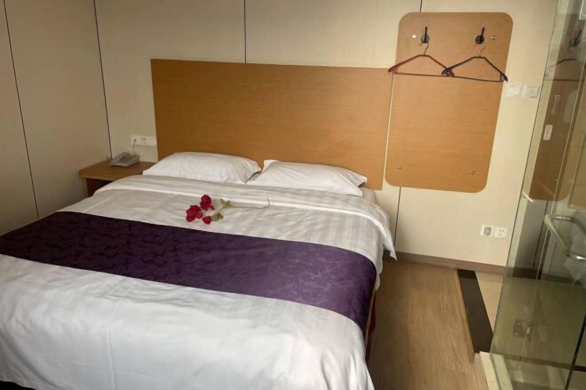 Habitación de hotel con cama, cabecera de madera, mesita de noche con teléfono y mampara de vidrio.