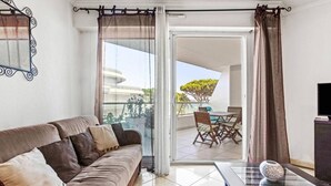 A modern living room with a sofa, a glass coffee table, and a view of a balcony with outdoor furniture.