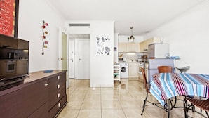 A compact living space with a kitchenette, a dining area with a striped tablecloth, and a television on a cabinet.