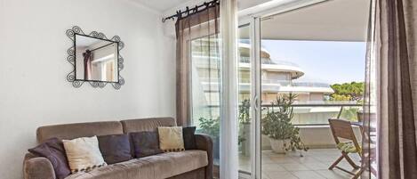 A modern living room with a sofa, a mirror, and a balcony with a view of a building.