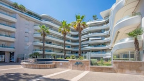A modern multi-story hotel with a curved facade, palm trees, and a clear blue sky.
