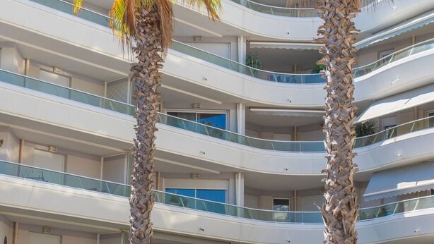 A multi-story hotel with balconies, palm trees, and a modern architectural design.