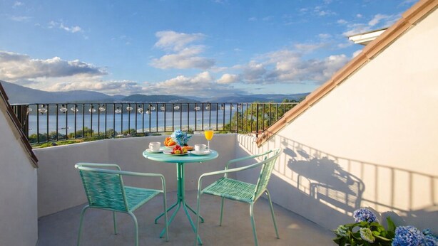 A balcony with a table and chairs, overlooking a body of water and mountains.